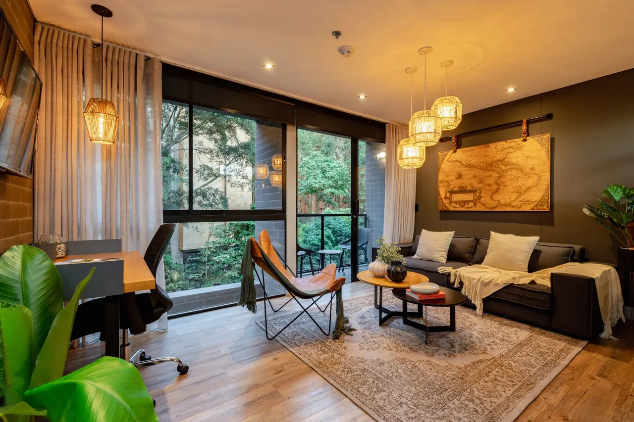 Living room of a furnished apartment at Loma Verde in El Poblado, Medellín, with sofa, work desk and balcony overlooking the greenery